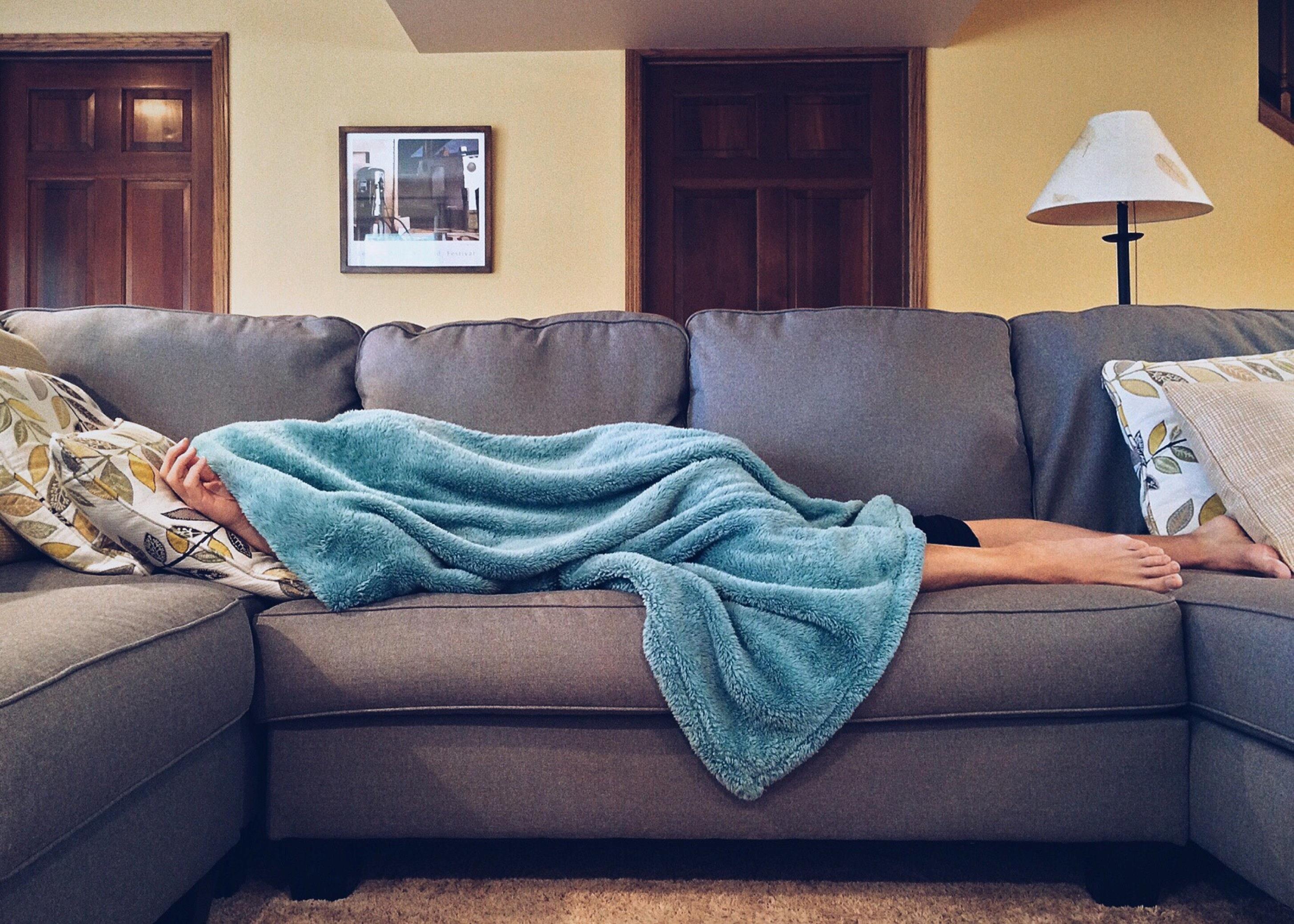 Muž leží nemocný doma na gauči. Je po hlavu přikrytý dekou, není mu dobře.
